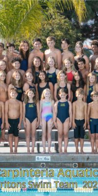 Swimmers stand on bleachers near pool edge for team photo